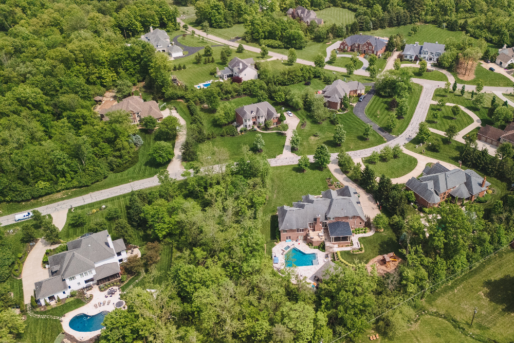 Indian Hill Ohio - Elegant Outdoor Lighting Design Aerial view of a suburban neighborhood with curved roads, green lawns, and two houses with swimming pools.