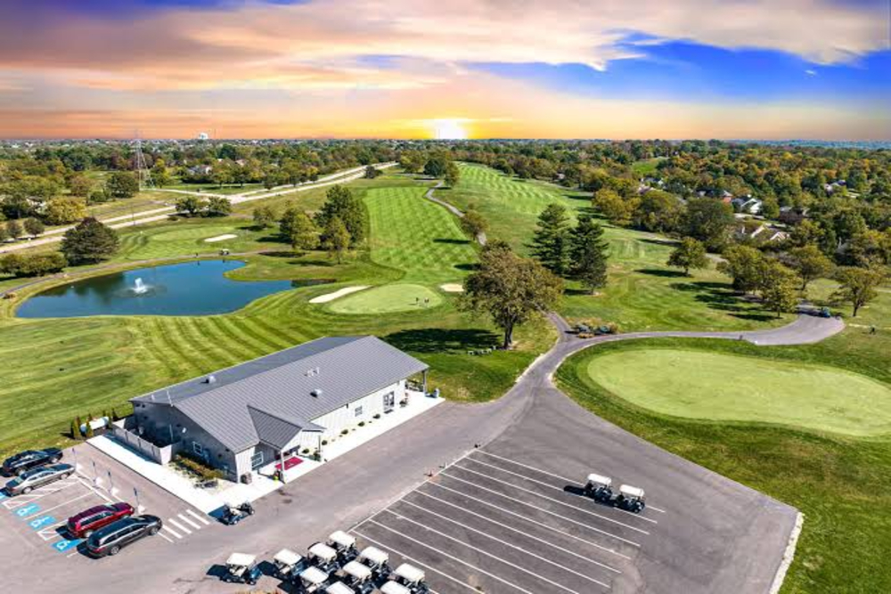 Beckett Ridge - Elegant Outdoor Lighting Design Aerial view of a golf course with a clubhouse, parking lot, ponds, and multiple greens at sunset.